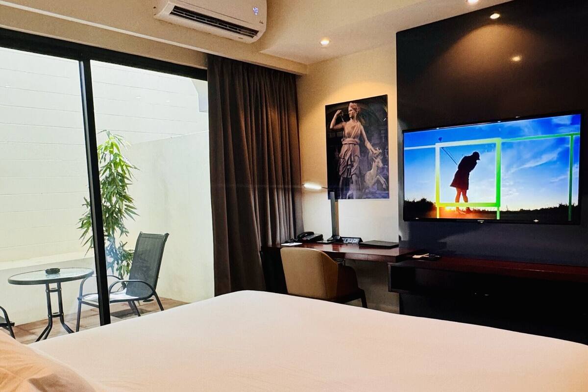A hotel room with a large bed, a desk with a chair, a television, and a window with curtains.