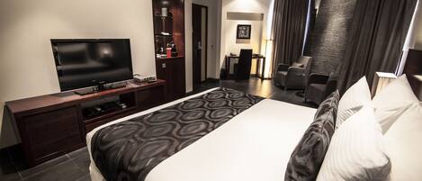 A modern hotel room with a large bed, a flat-screen TV, a desk, and a seating area with chairs.