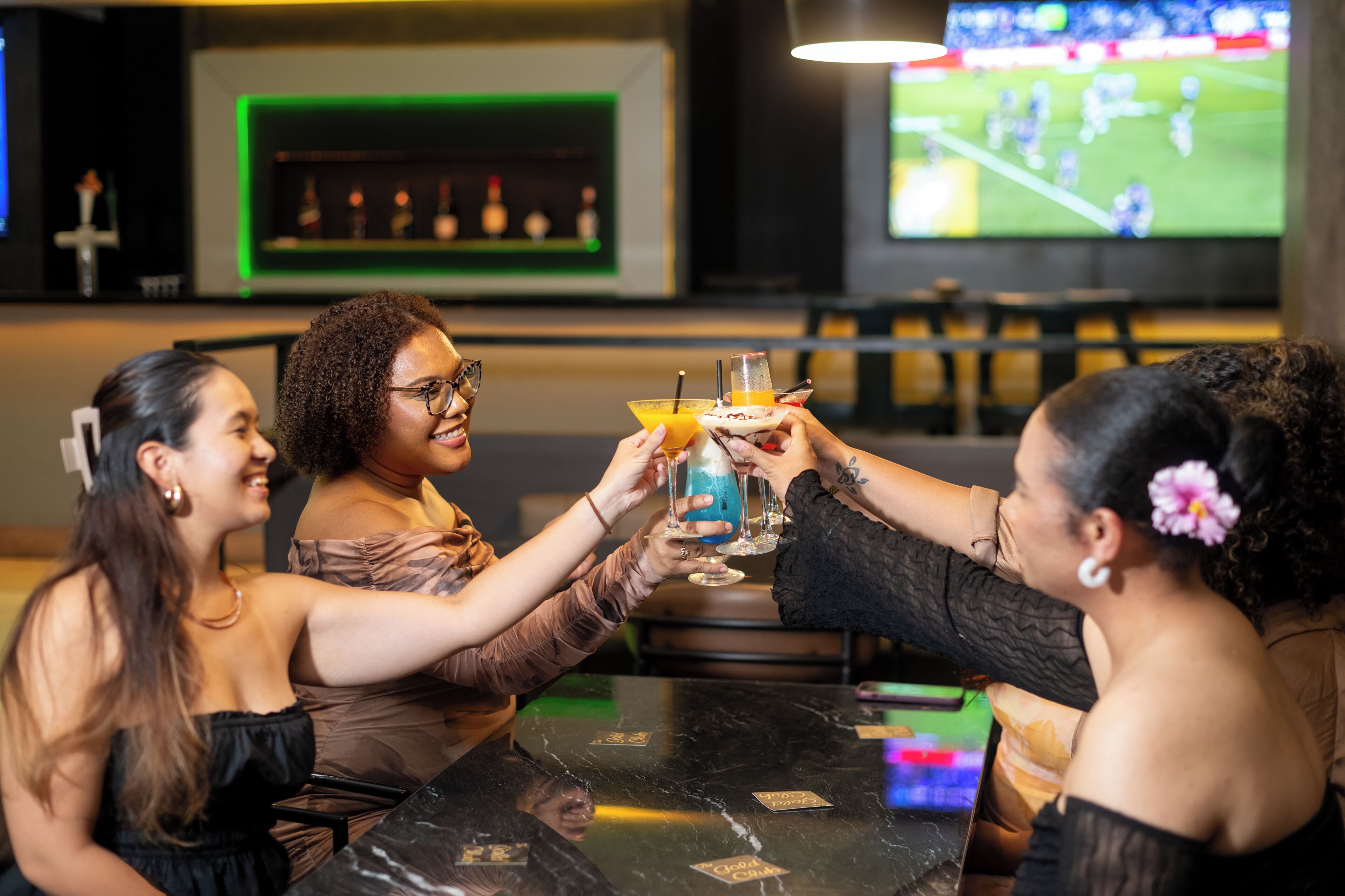 Een groep mensen die proosten in een bar, met een sportwedstrijd op de televisie op de achtergrond.