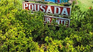 A sign with colorful text and a parrot illustration, surrounded by lush greenery. - Enseada do Espelho (Porto Seguro)