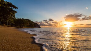 A beach with a sunset, calm waves, and a forested area. - Enseada do Espelho (Porto Seguro)