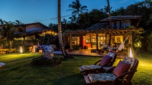 A resort with a covered outdoor seating area, palm trees, and a sign for a restaurant. - Enseada do Espelho (Porto Seguro)