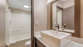 Une salle de bain moderne avec une baignoire, des toilettes et un grand lavabo surmonté d’un miroir.