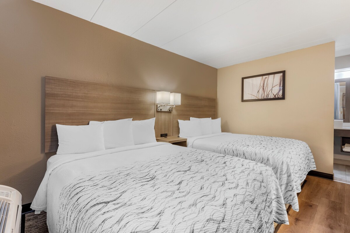 A hotel room with two beds, a wooden headboard, a nightstand with a lamp, and a framed picture on the wall.