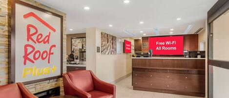 A hotel lobby with a reception desk, Red Roof Plus signage, and a Red Roof Plus Plus sign.