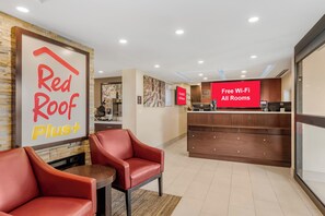 A hotel lobby with a reception desk, Red Roof Plus signage, and a Red Roof Plus Plus sign.