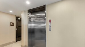 Un ascensor con detalles metálicos, un botón de emergencia contra incendios y un letrero de baño de mujeres en la pared.