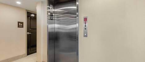 An elevator with a metallic finish, a fire recall button, and a women restroom sign on the wall.