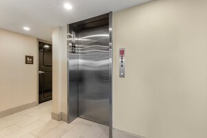 Un ascensor con detalles metálicos, un botón de emergencia contra incendios y un letrero de baño de mujeres en la pared.