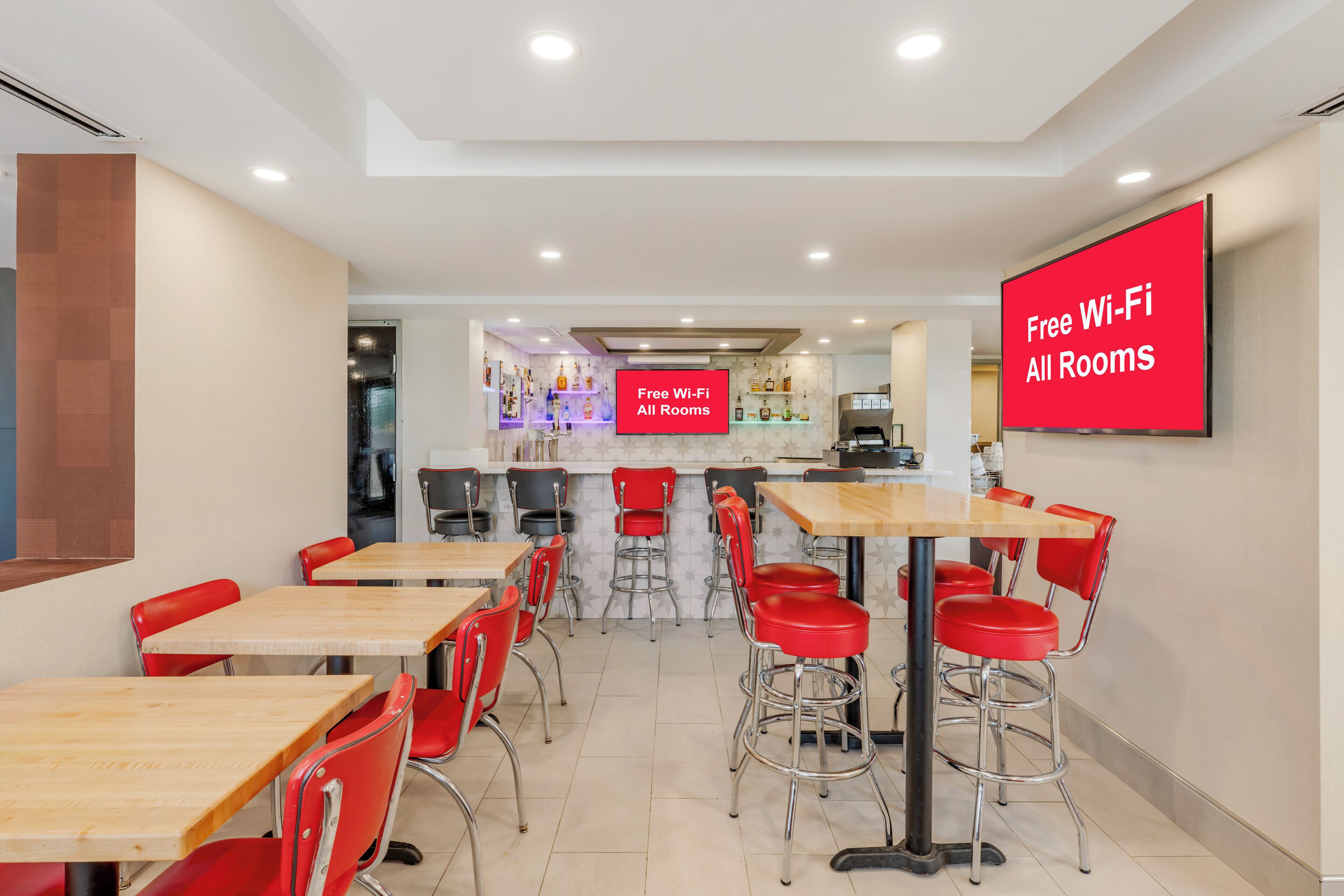 A modern dining area with multiple tables and red chairs, a bar area in the background, and a sign indicating free Wi-Fi availability.