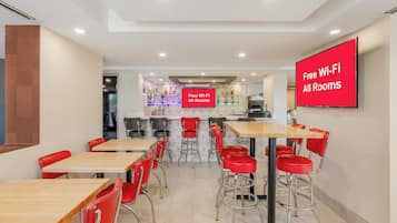 A modern dining area with multiple tables and red chairs, a bar area in the background, and a sign indicating free Wi-Fi availability.