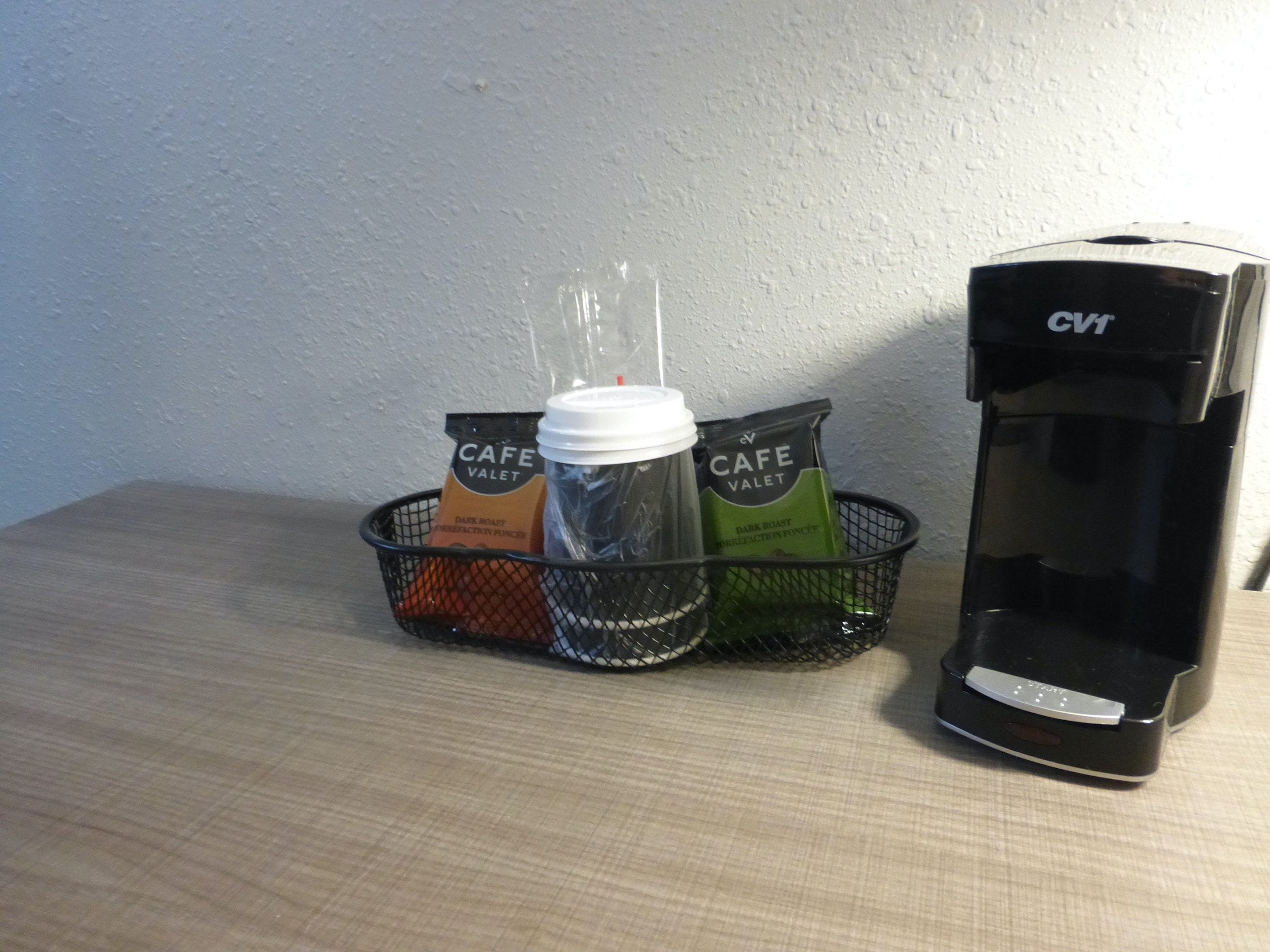 A coffee maker, a basket with a coffee cup, and two packets of Cafe Valet coffee on a table.