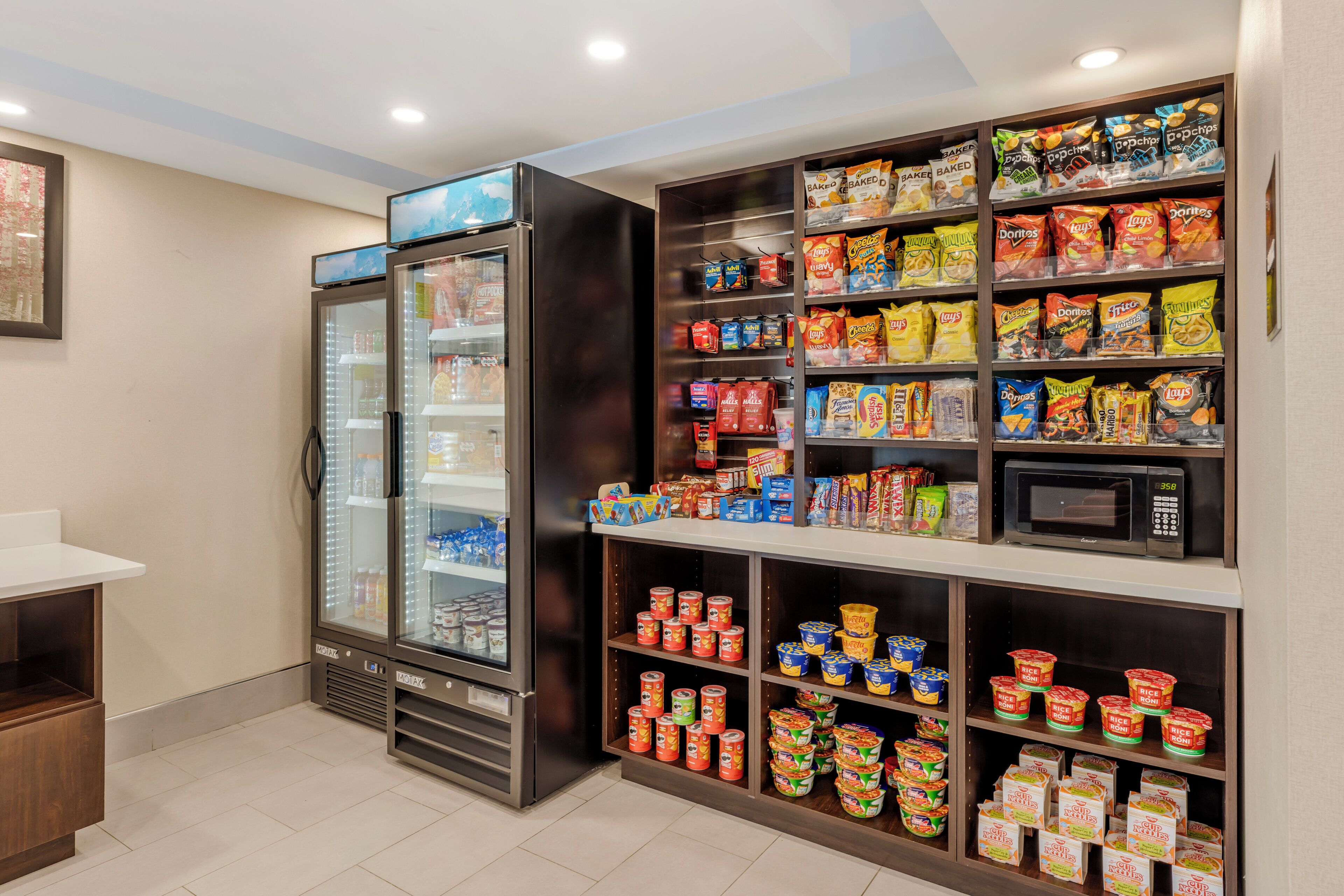 A snack and beverage section with a refrigerated display, microwave, and various packaged foods.