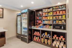 Una sección de aperitivos y bebidas con mostrador refrigerado, microondas y diversas opciones de comida envasada.