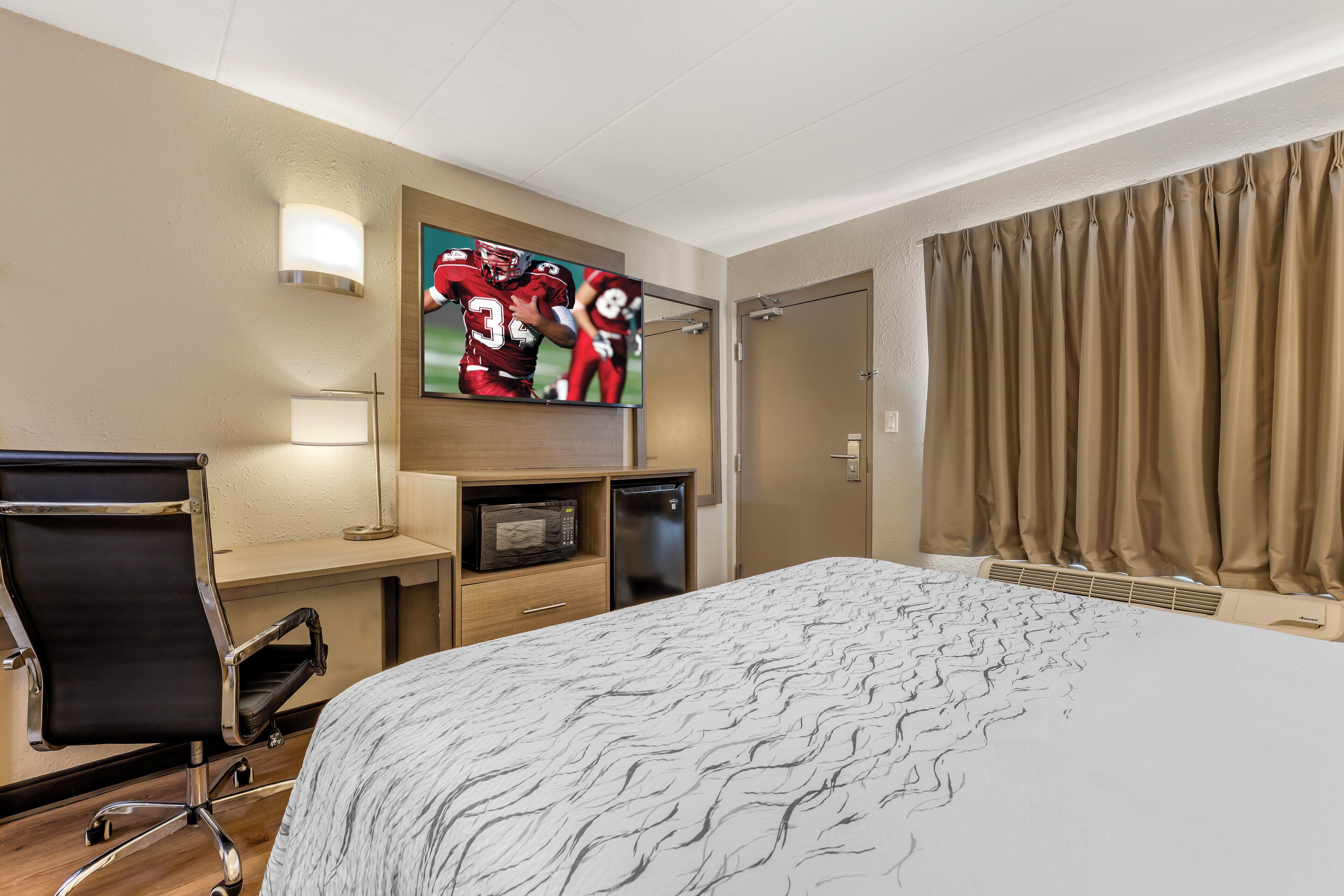 Habitación de hotel con cama, escritorio con silla, televisor, microondas y puerta.