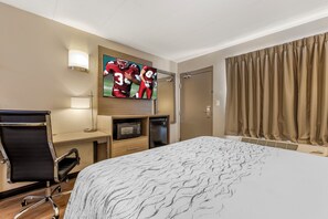 Habitación de hotel con cama, escritorio con silla, televisor, microondas y puerta.