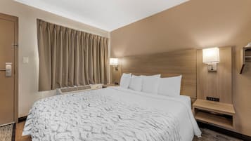 A hotel room with a large bed, a headboard with integrated lighting, a bedside table, and a window with curtains.