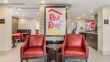 Un área de descanso Red Roof Plus con sillones de cuero, una pequeña mesa y una pared decorativa de piedra.