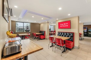 Un restaurante moderno con asientos rojos y negros, un tablero de menú visible y un letrero que indica disponibilidad de Wi-Fi gratuito.