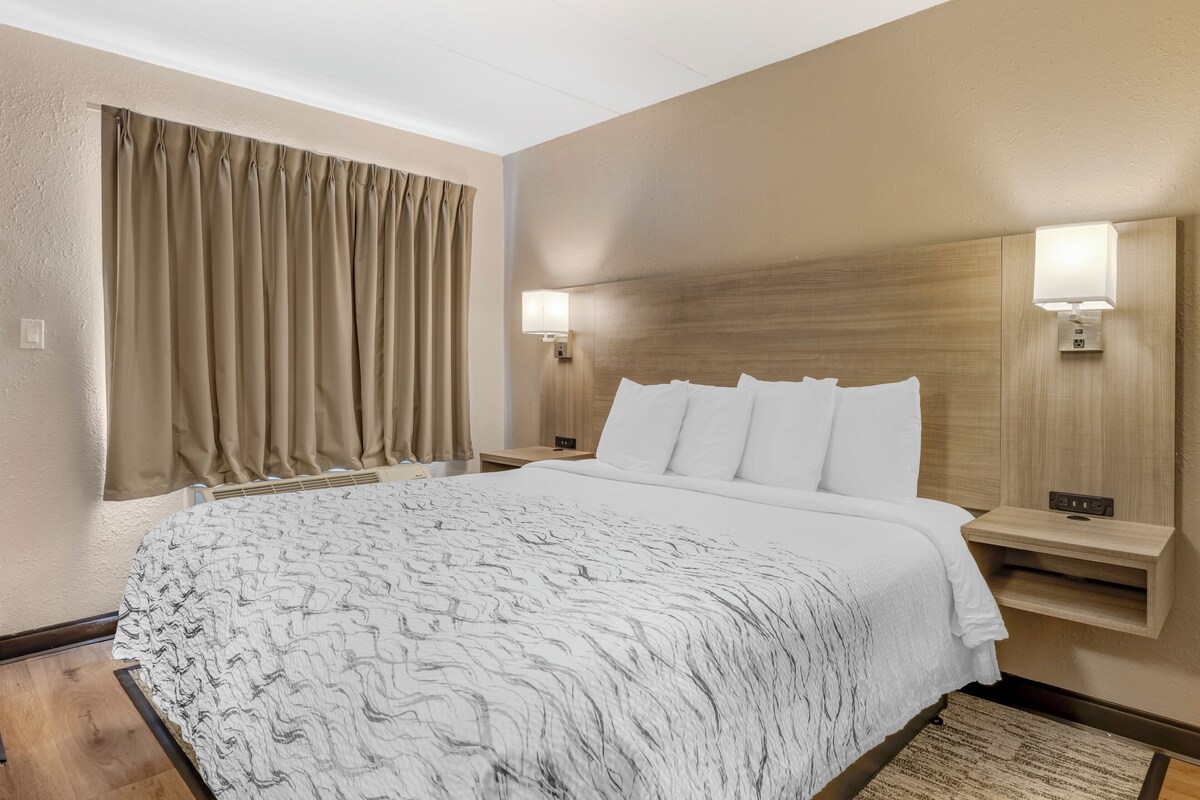 A hotel room with a large bed, two bedside tables with lamps, a wooden headboard, and a window with curtains.