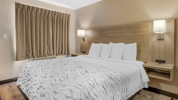 Una habitación de hotel con una cama grande, dos mesitas de noche, un cabecero y una ventana con cortinas.