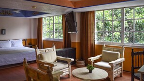 Una habitación de hotel con una cama, dos sillones, una mesita y un televisor.
