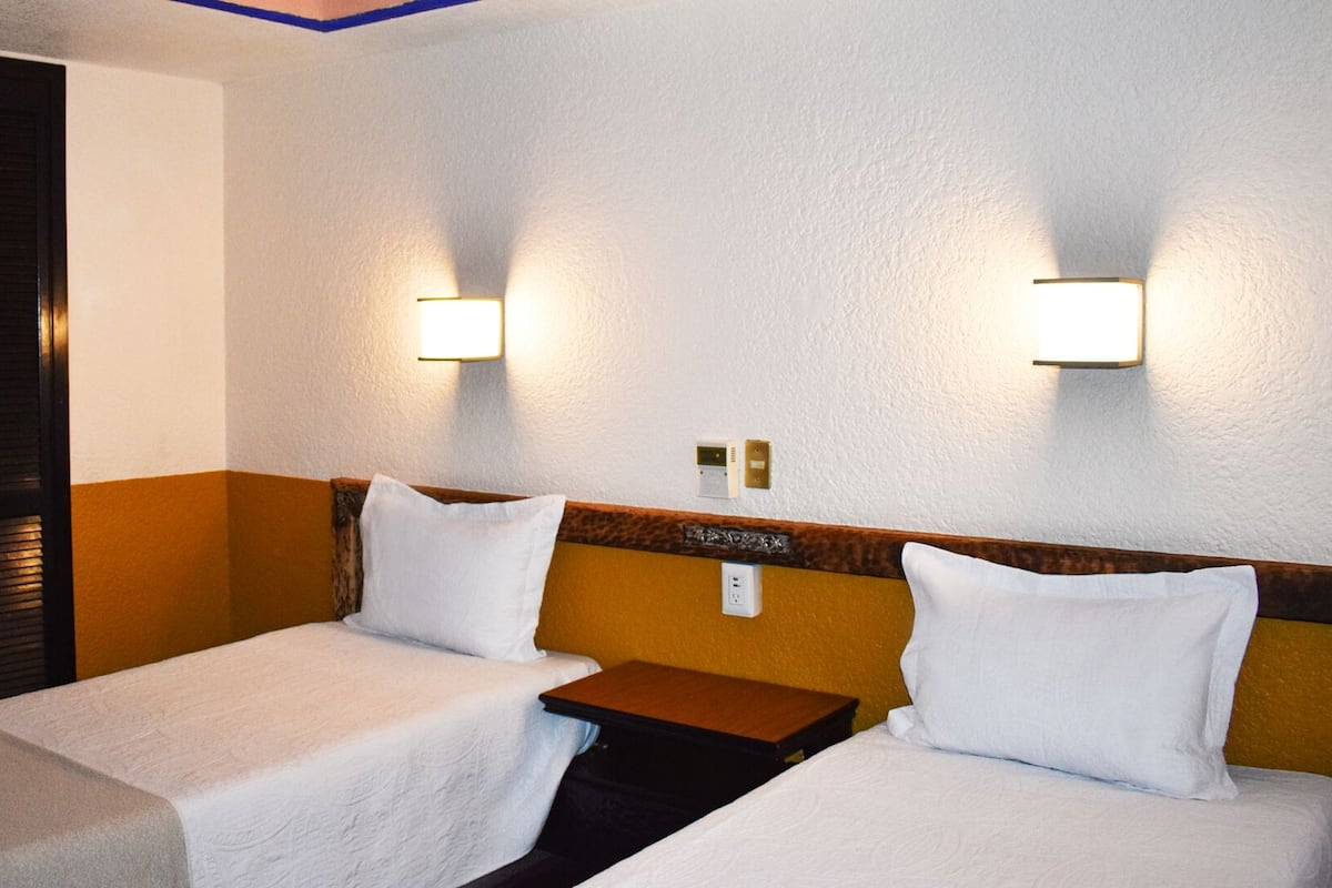 A hotel room with two single beds, a wooden headboard, a nightstand, and two wall-mounted light fixtures.