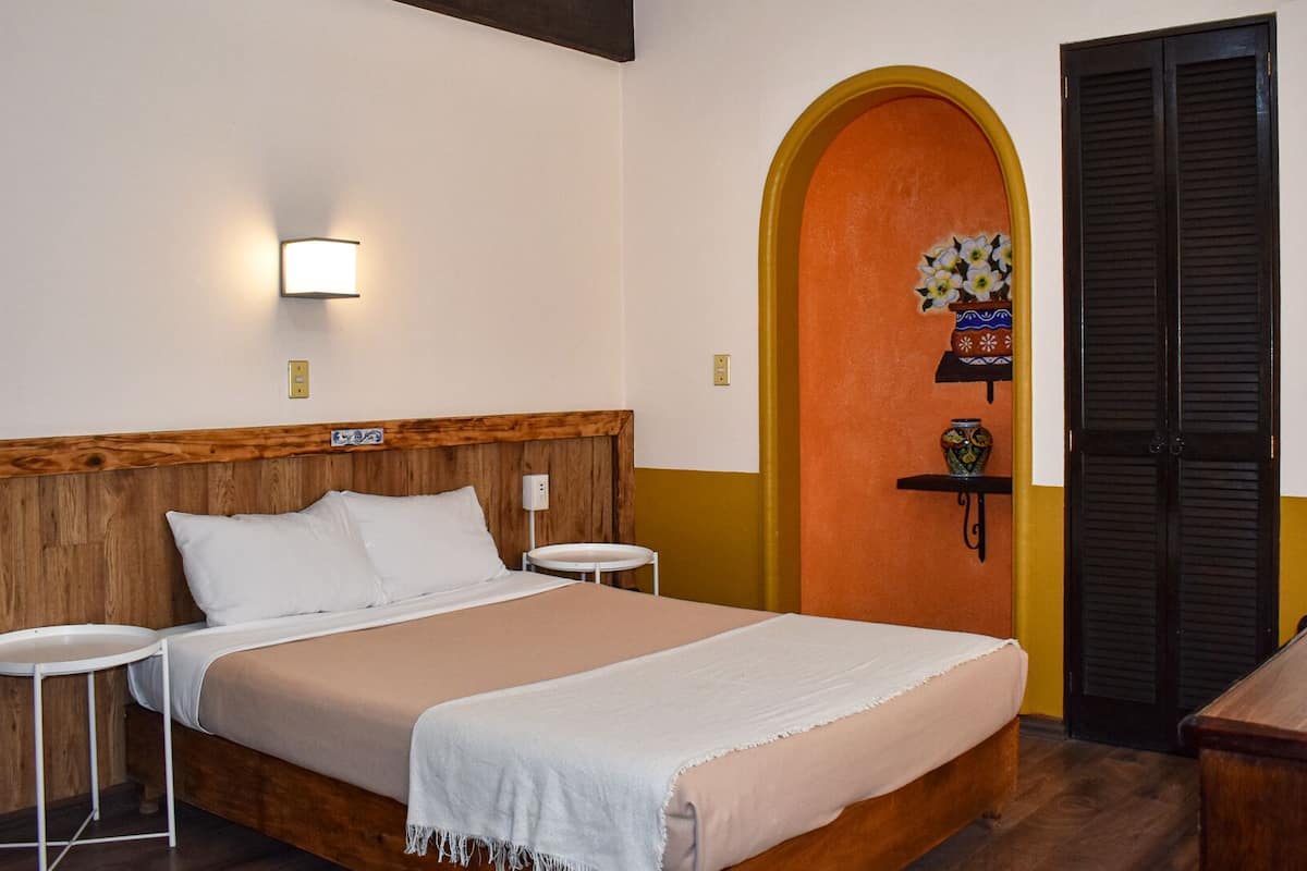 A hotel room with a wooden headboard bed, two bedside tables, a TV, and a door with a decorative arch.