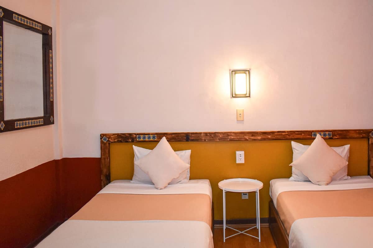A hotel room with two beds, a small stool, a wall-mounted light, and a mirror.