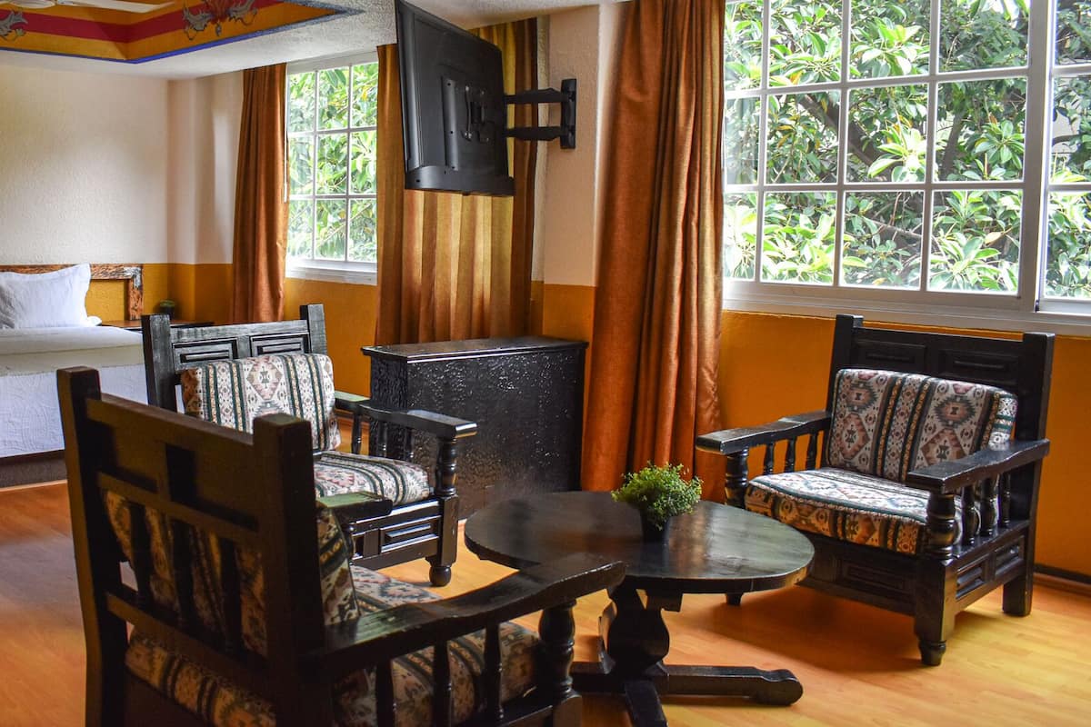 A hotel room with a bed, two armchairs, a small table, and a TV mounted on the wall.