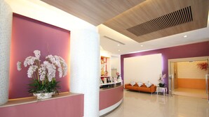 A reception area with a curved reception desk, a potted orchid plant, an orange sofa, and a glass door leading to another room. - The Icon Place at Central Pattaya (Pattaya)