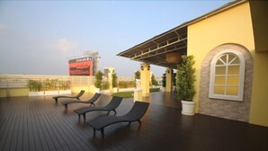 A rooftop deck with lounge chairs, a potted plant, and a building with a yellow facade and arched window. - The Icon Place at Central Pattaya (Pattaya)