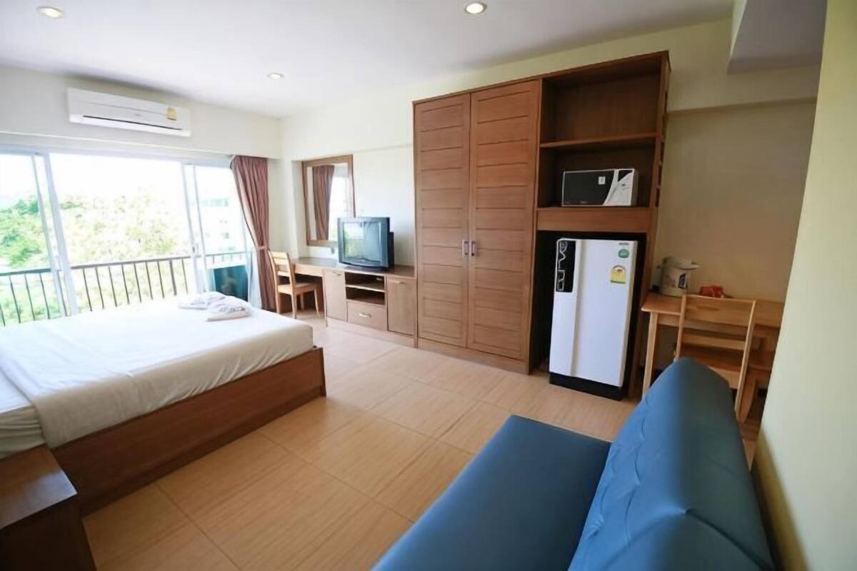 A hotel room with a bed, a desk, a television, a wardrobe, and a refrigerator.