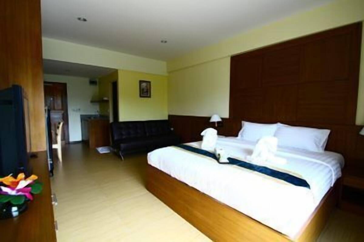 A hotel room with a large bed, a wooden headboard, a bedside table with a lamp, and a view of the hallway.