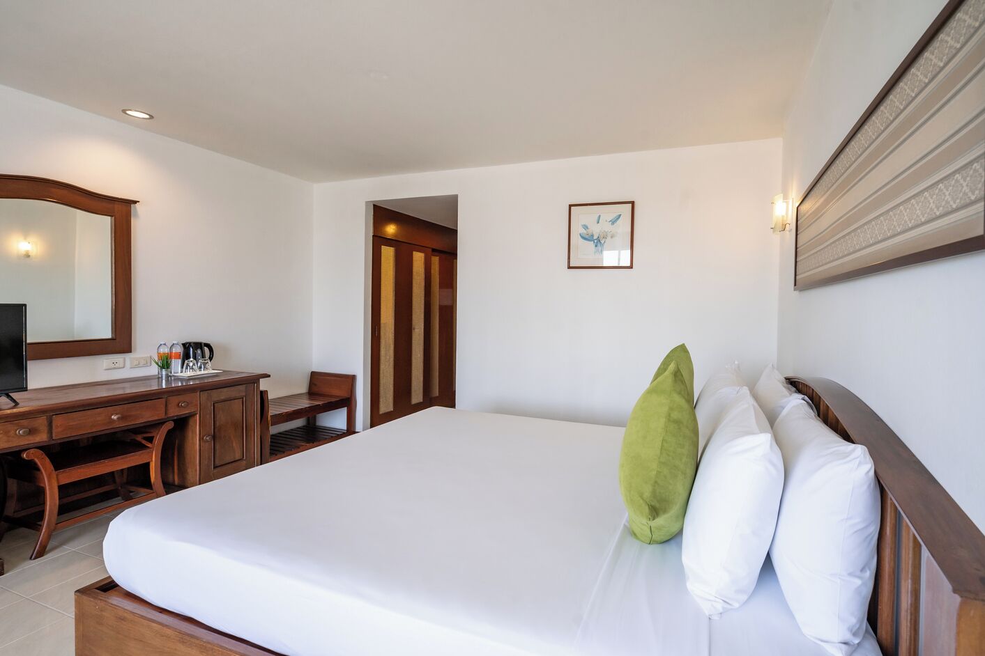 A hotel room with a large bed, a desk with a chair, a mirror, and a framed picture on the wall.