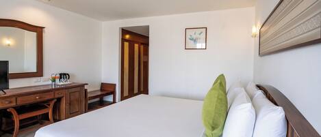 A hotel room with a large bed, a desk with a chair, a mirror, and a framed picture on the wall.