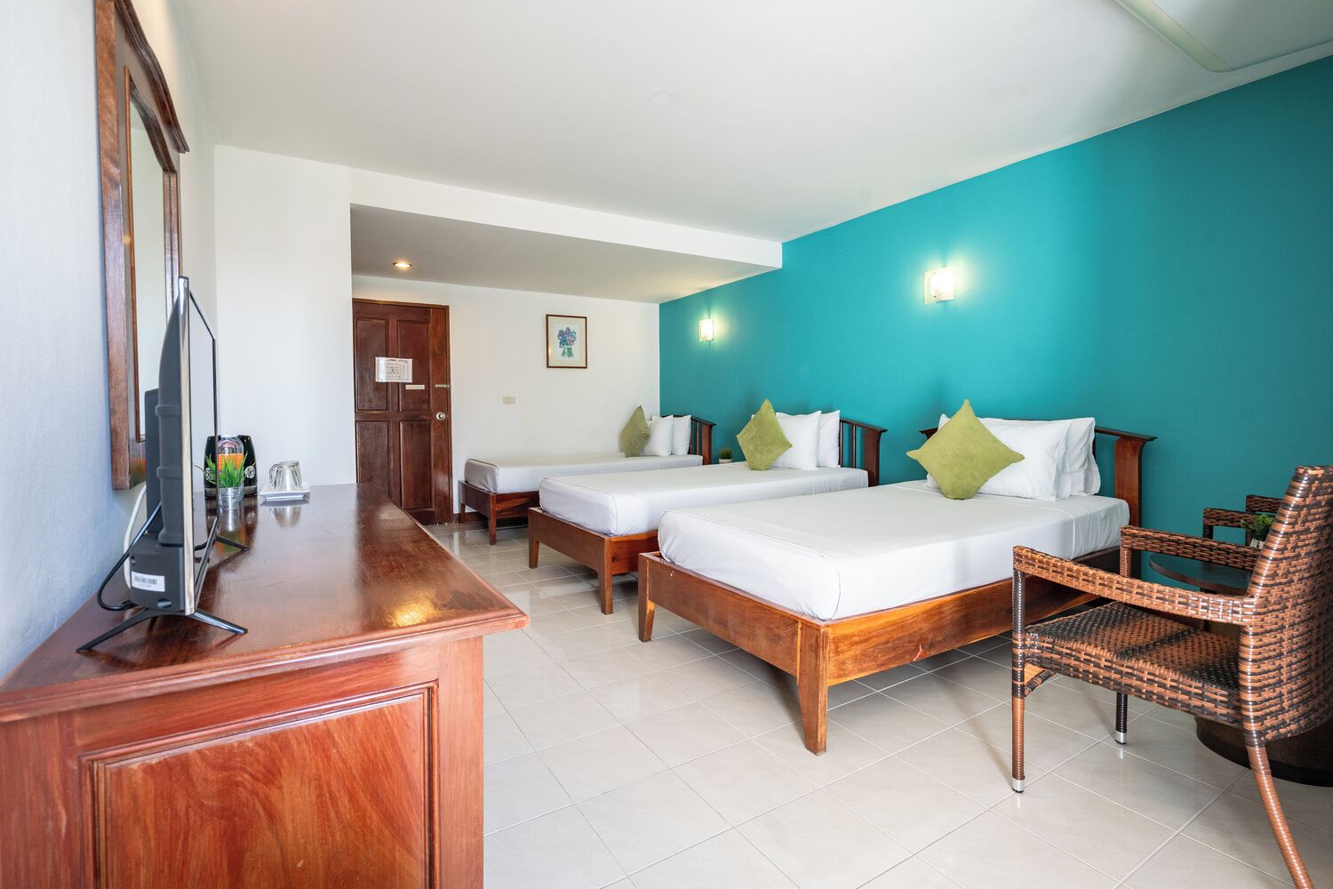 Une chambre d’hôtel avec deux lits en bois, un bureau en bois, une chaise en osier et un téléviseur posé sur un meuble.