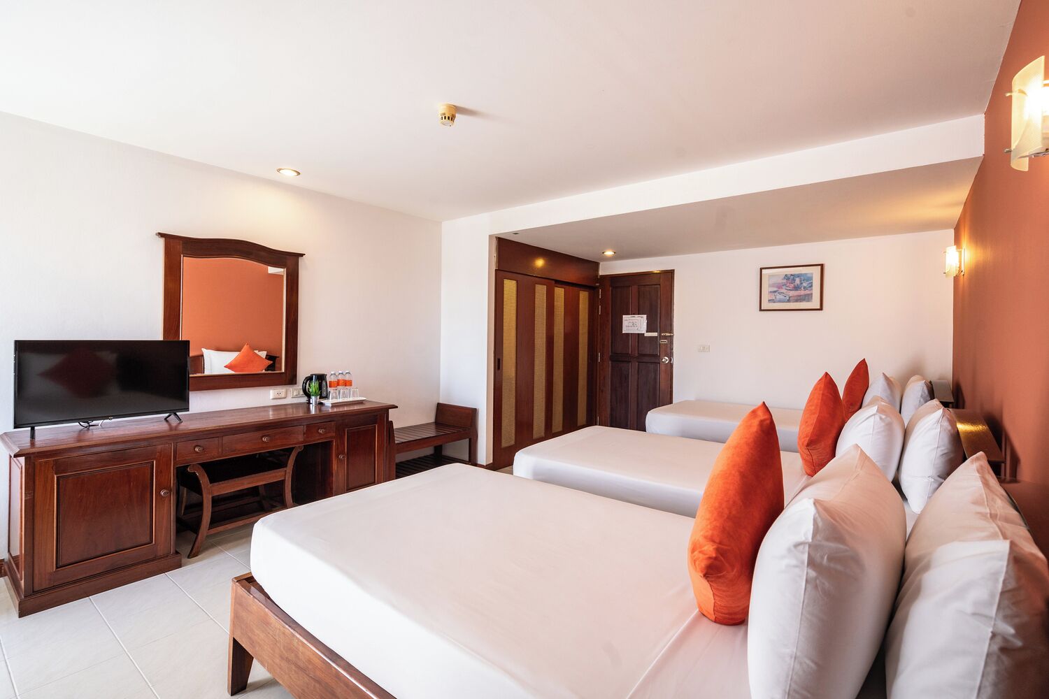 A hotel room with two beds, a desk with a television, a mirror, and a door leading to another room.