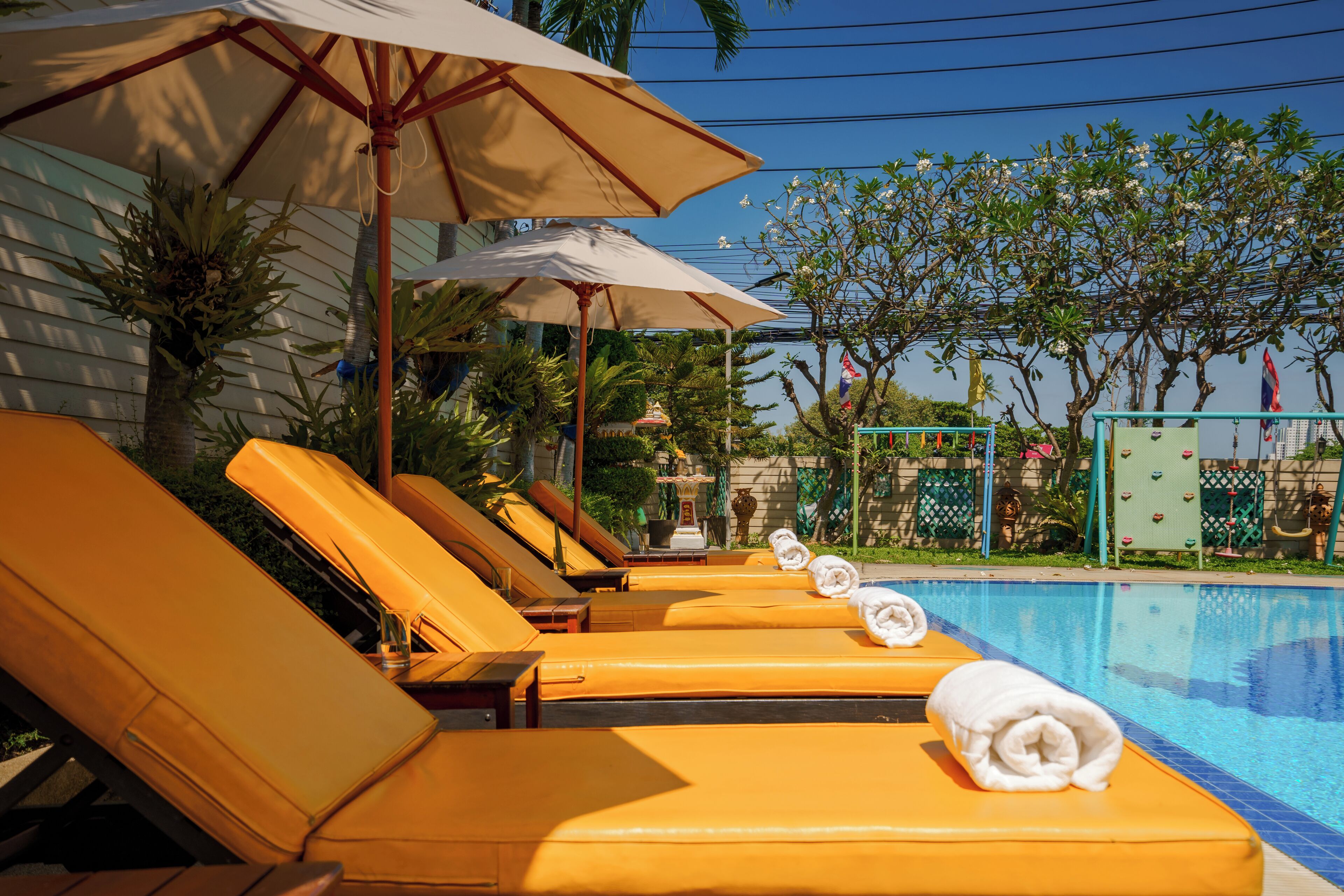 A poolside area with sun loungers and umbrellas, a clear blue pool, and a tropical garden backdrop.
