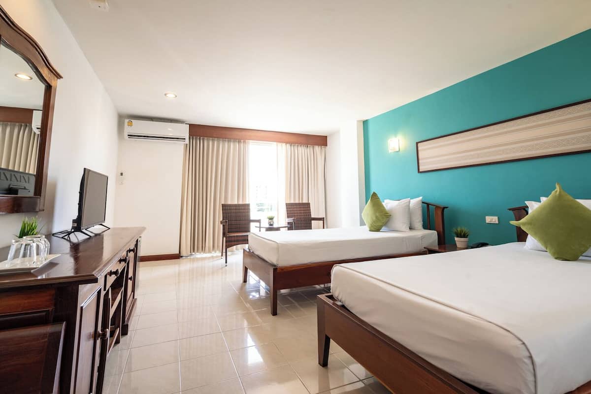 Habitación de hotel con dos camas, un escritorio con televisor y un ventanal grande con cortinas.