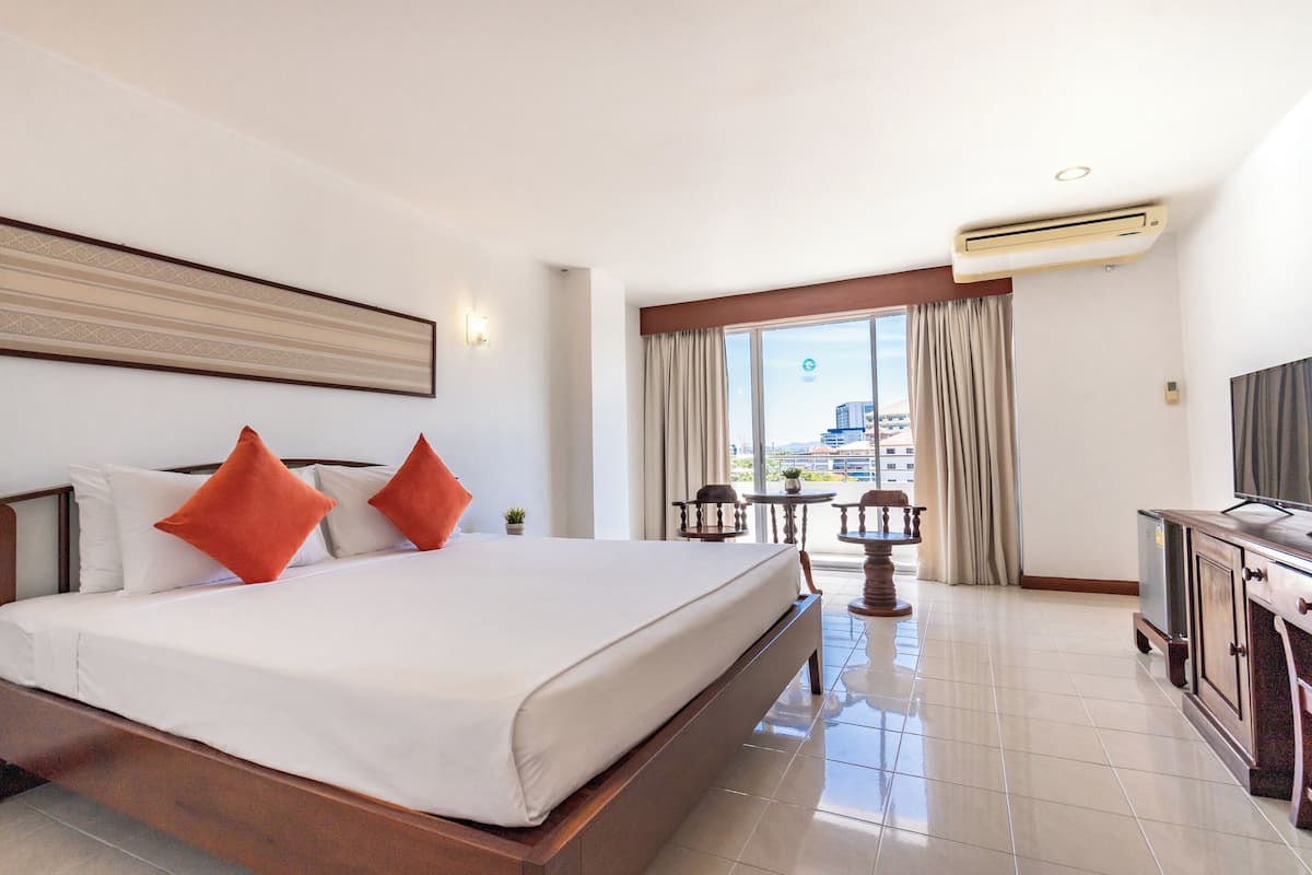 Habitación de hotel con una cama grande, televisión, escritorio y balcón con cortinas.