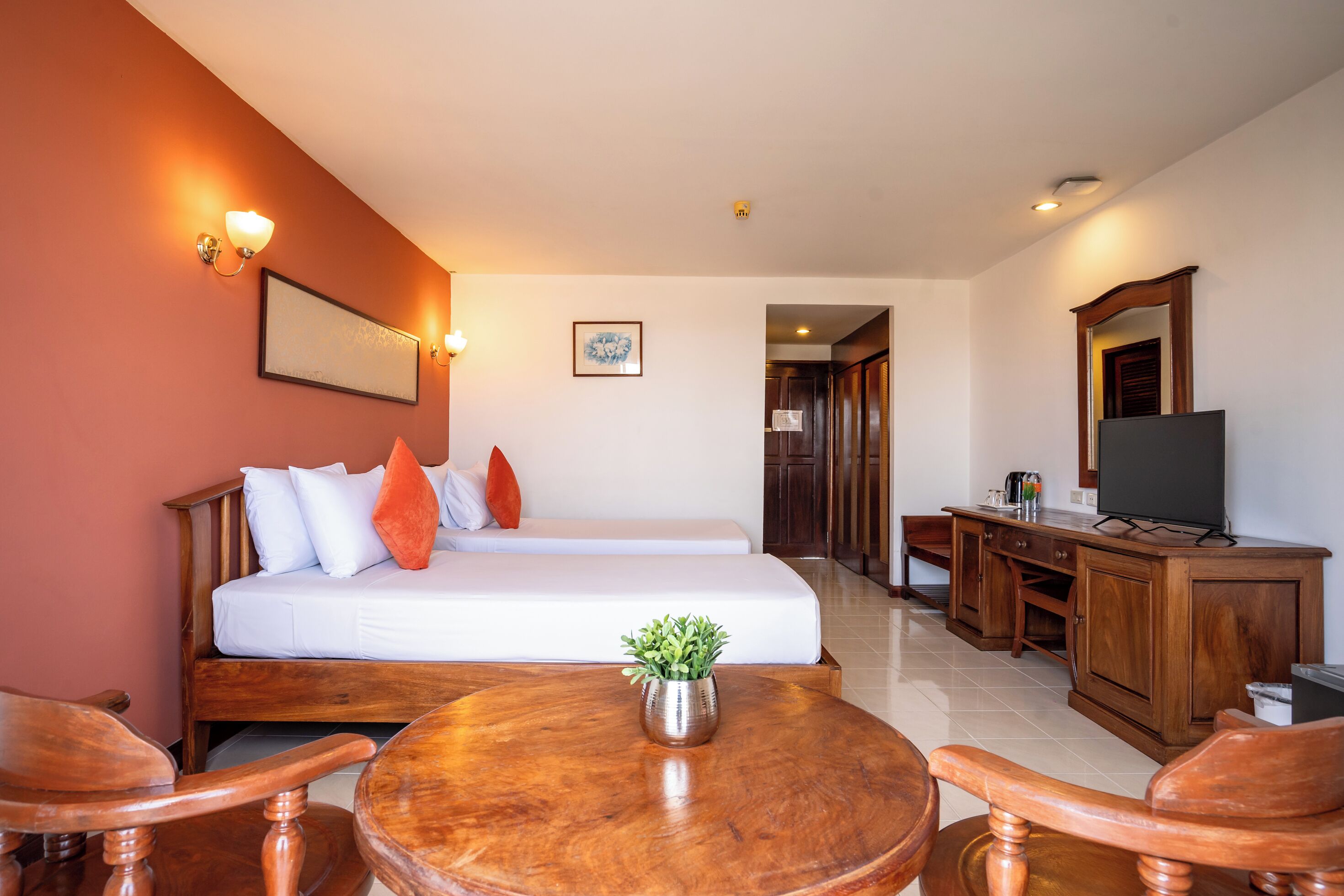 A hotel room with a bed, bedside table, TV, and a small plant.