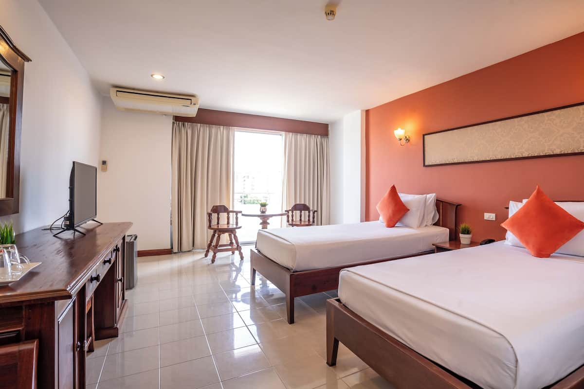 Habitación de hotel con dos camas, un escritorio con televisor, una mesita con sillas y una ventana con cortinas.
