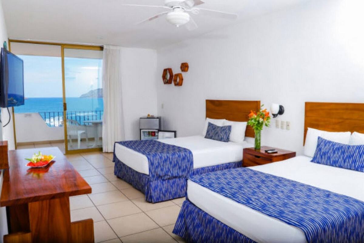 A hotel room with two beds, a desk, a TV, and a balcony with a view.