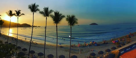 Una playa con palmeras, sombrillas y una puesta de sol.
