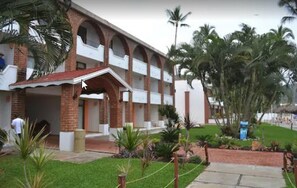 A multi-story building with a covered entrance, brick walls, and a well-maintained garden with palm trees.