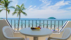 Un balcón con una mesa y dos sillas, con vista a una playa con palmeras y cielo despejado.
