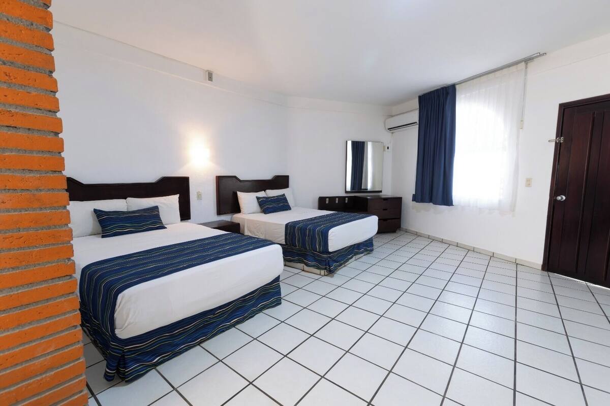 A hotel room with two beds, a dresser, a mirror, and a door.