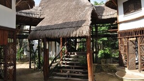Una estructura tradicional con techo de paja y escaleras de madera que conducen a una plataforma, rodeada de vegetación natural.