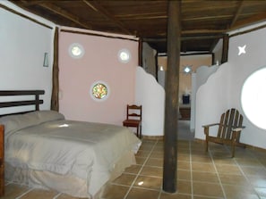 Ein Schlafzimmer mit Bett, Stuhl, einem Holzbalken, einer Wand mit runden Fenstern und einer sternförmigen Leuchte.